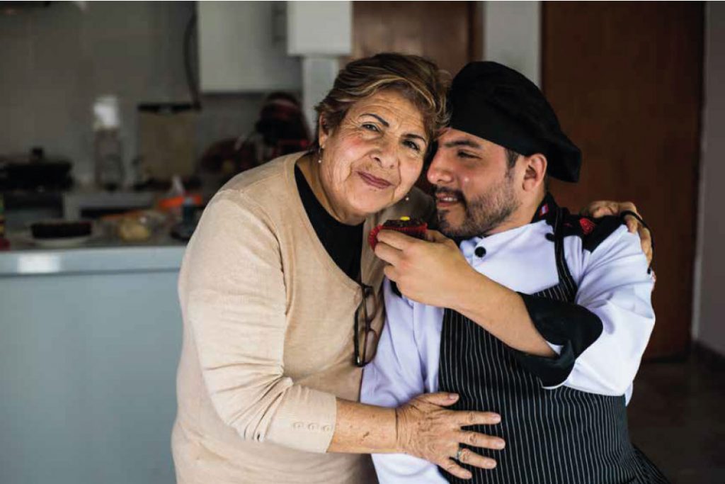 emprendedor con discapacidad del rubro de la pastelería sosteniendo un pastel y abrazando a su madre