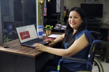 mujer usuaria de silla de ruedas usando una computadora con la página web del registro nacional del conadis